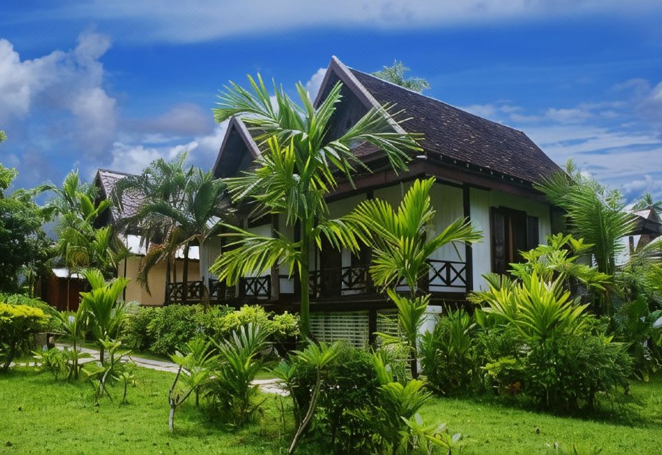 Steep-roofed guest buildings set among lawn and palms under a blue sky