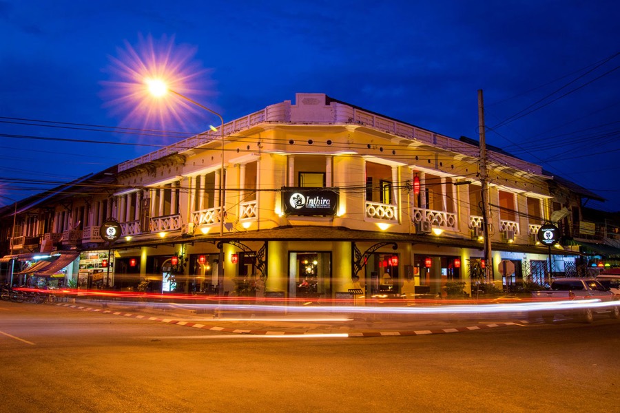 A two-storey French colonial corner building lit at night, with a columned upper balcony