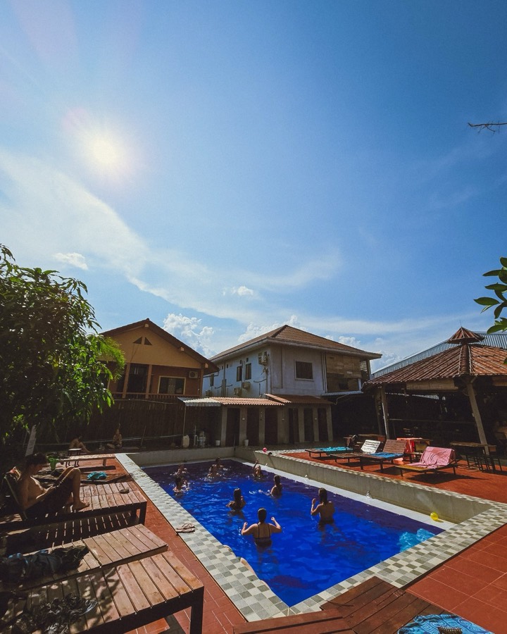 A small blue pool in a tiled courtyard with wooden loungers, enclosed by the hostel buildings
