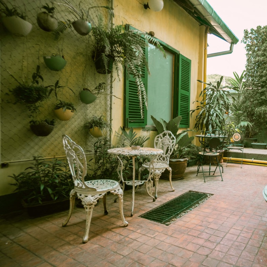 A brick-paved courtyard with white cast-iron tables beside a yellow building with green shutters
