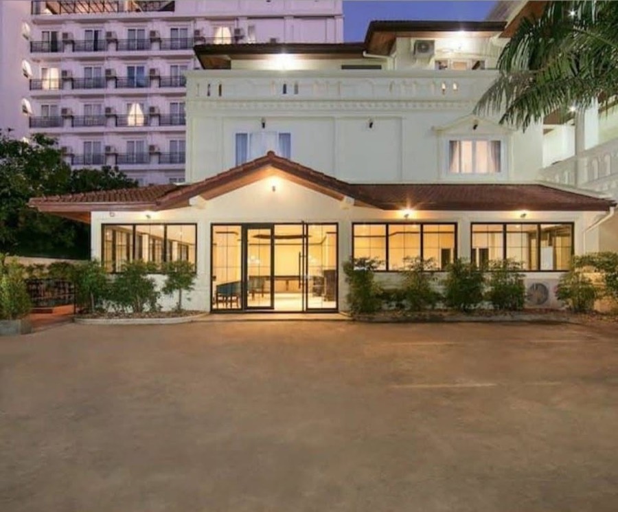 A white two-storey hotel lit at dusk, with a tiled porch roof over a glass-fronted lobby