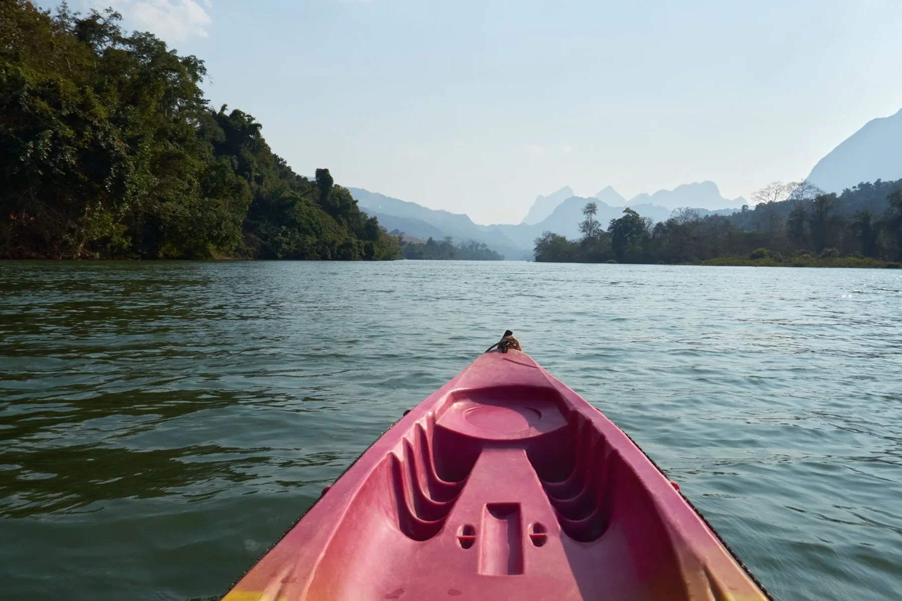 Kayaking on a calm river surrounded by green mountains in Laos